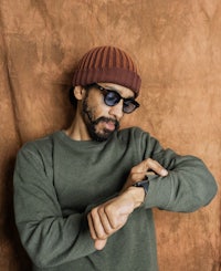 a man wearing sunglasses and a beanie is looking at his watch